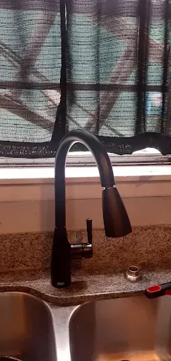 A modern black kitchen faucet with a pull-down sprayer installed in a countertop next to a sink in front of a window.