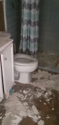 A white toilet in a bathroom with a blue chevron shower curtain and significant white debris covering the floor.