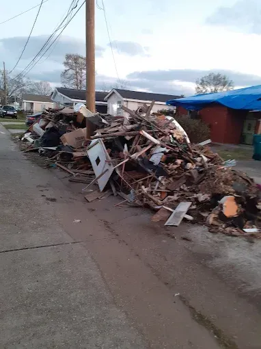 A large pile of storm debris consisting of wood, furniture, and building materials lining a residential street.