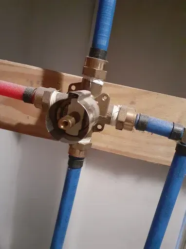 A brass shower mixing valve mounted to a wooden stud, connected to red and blue PEX plumbing pipes.
