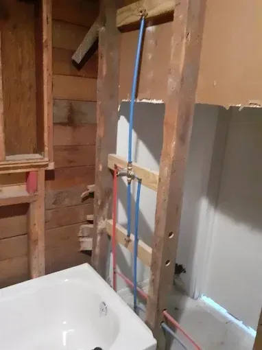 A residential bathroom renovation showing a shower faucet and PEX plumbing lines installed between wooden wall studs.
