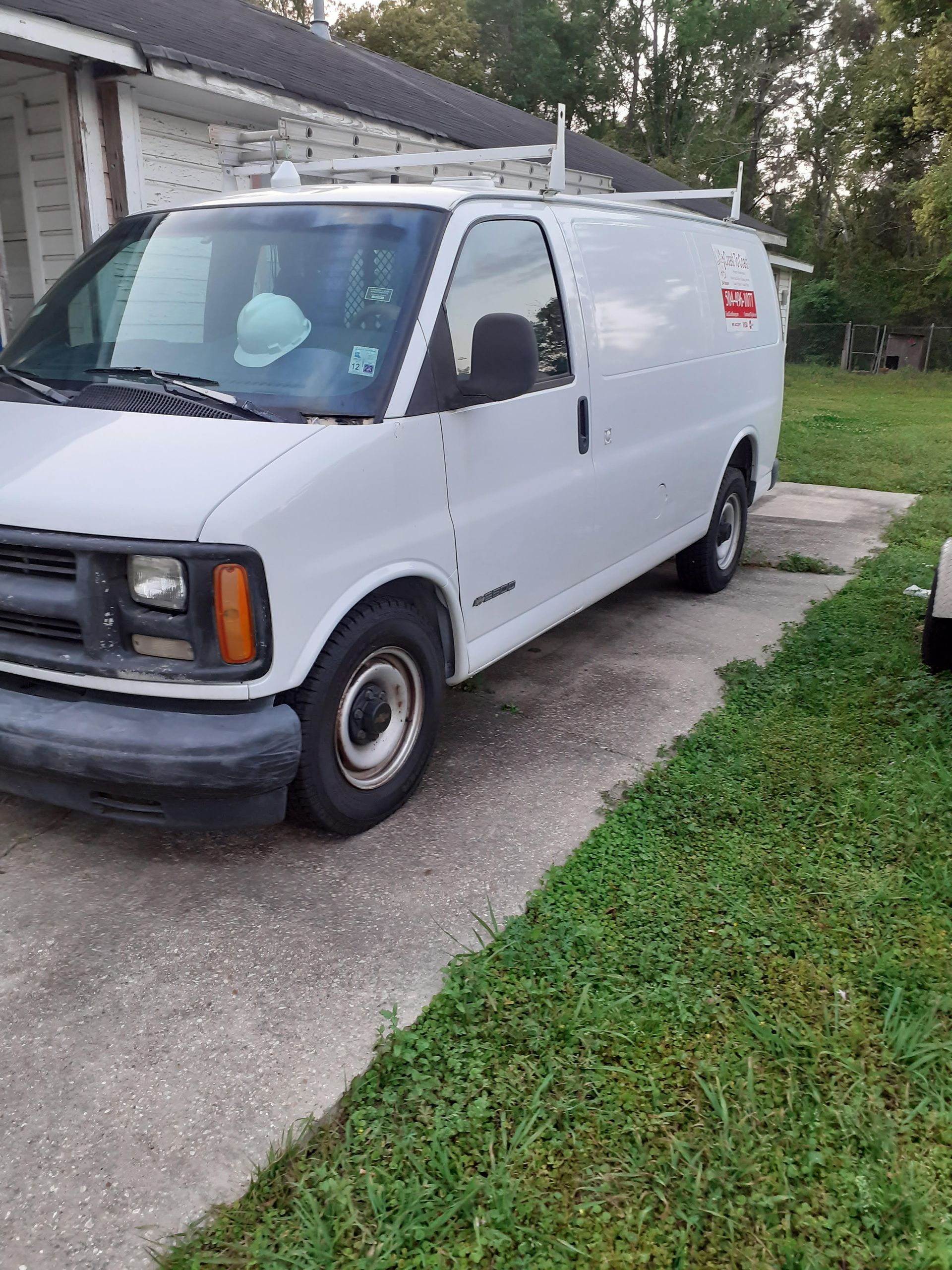 A white utility cargo van parked on a concrete driveway next to a grassy lawn.