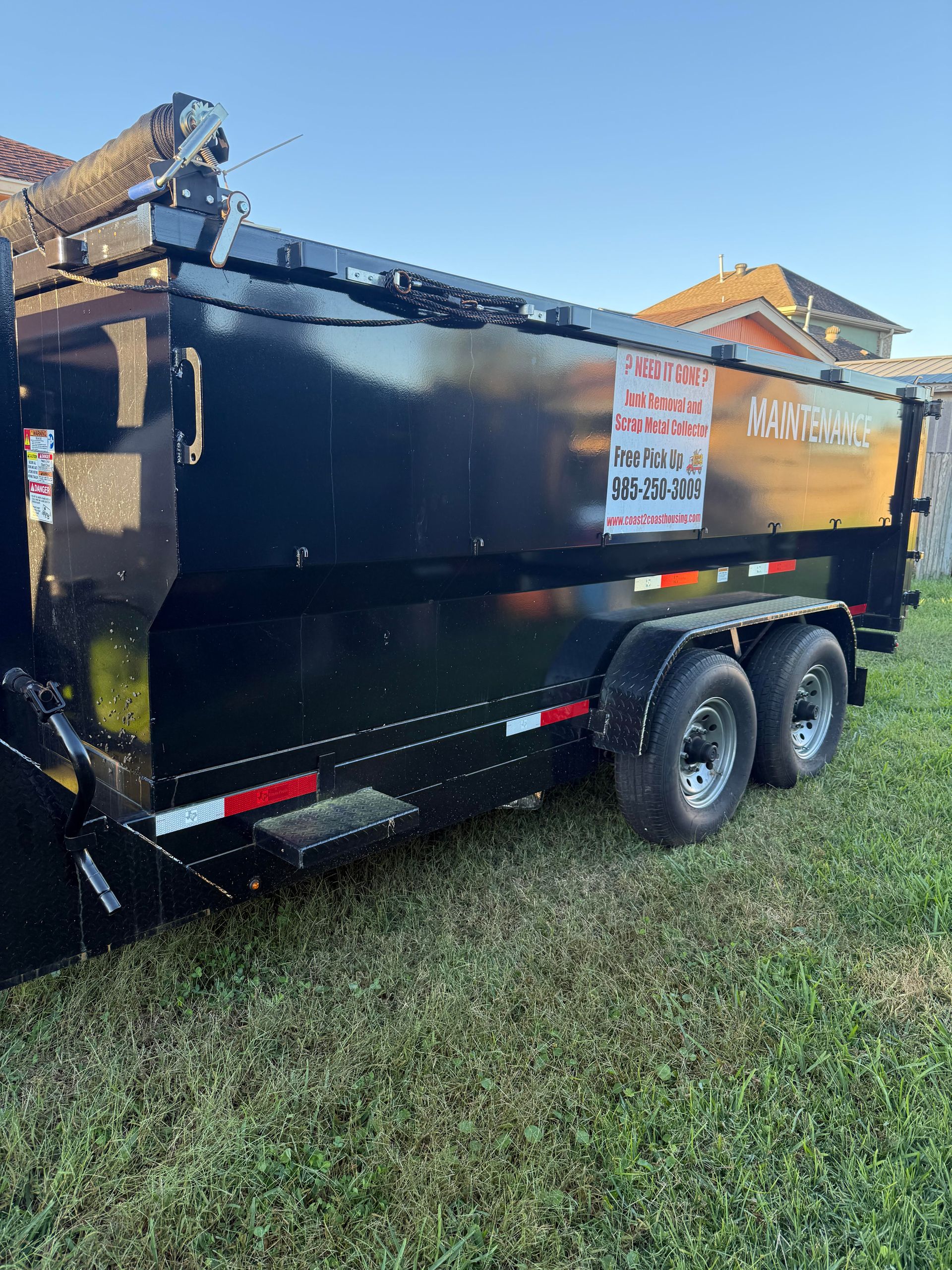 A black dump trailer parked on a grassy lawn under a clear blue sky.