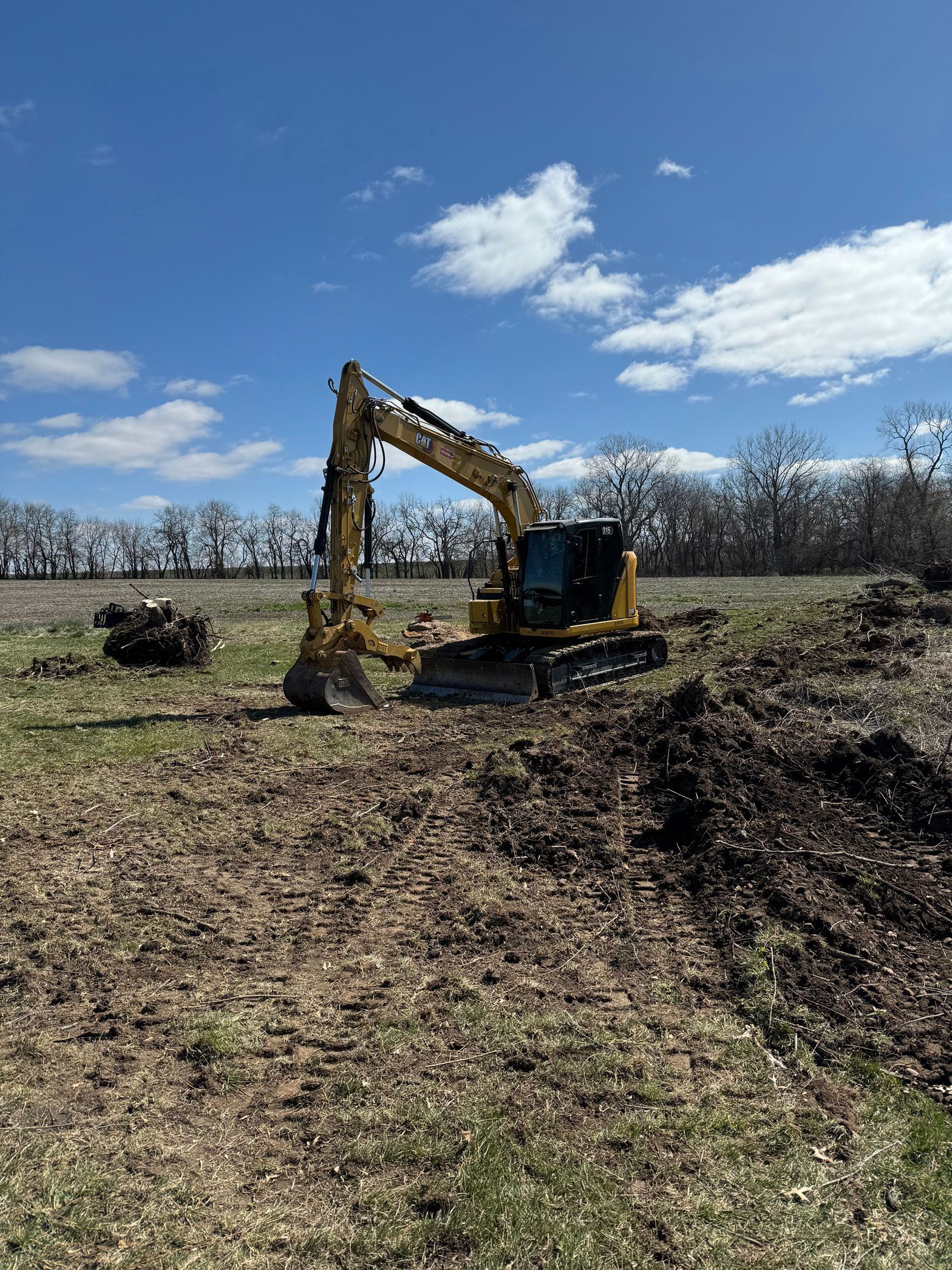 A yellow excavator is digging a hole in a field.