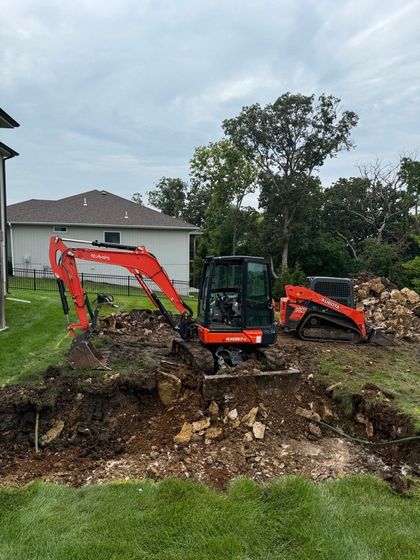 A couple of tractors are sitting on top of a dirt field in front of a house.