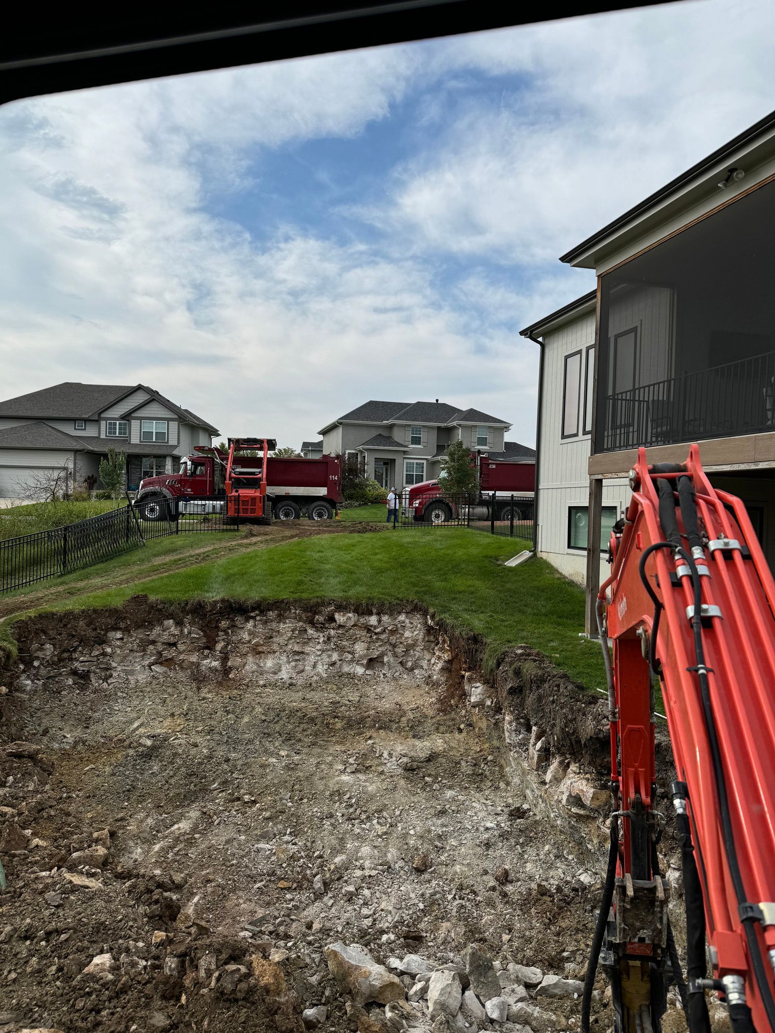 A large excavator is digging a hole in the ground in front of a house.