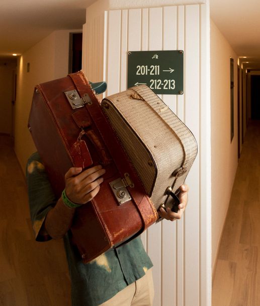 A man carrying two suitcases in front of a sign that says 201-211 212-213