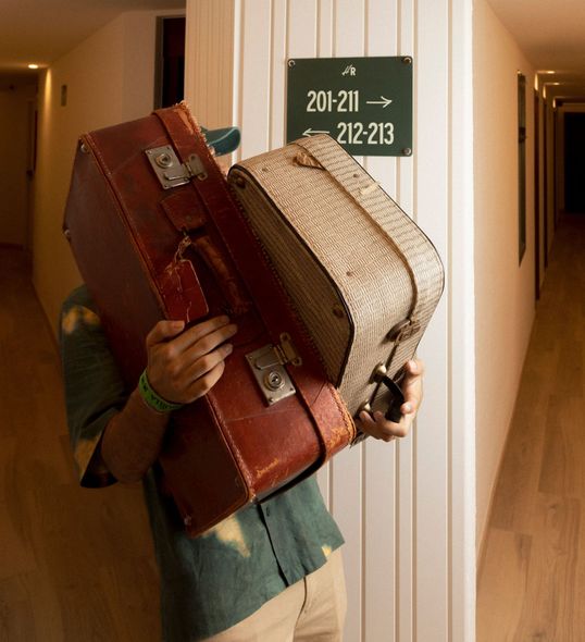 A man carrying two suitcases in front of a sign that says 201-211 212-213