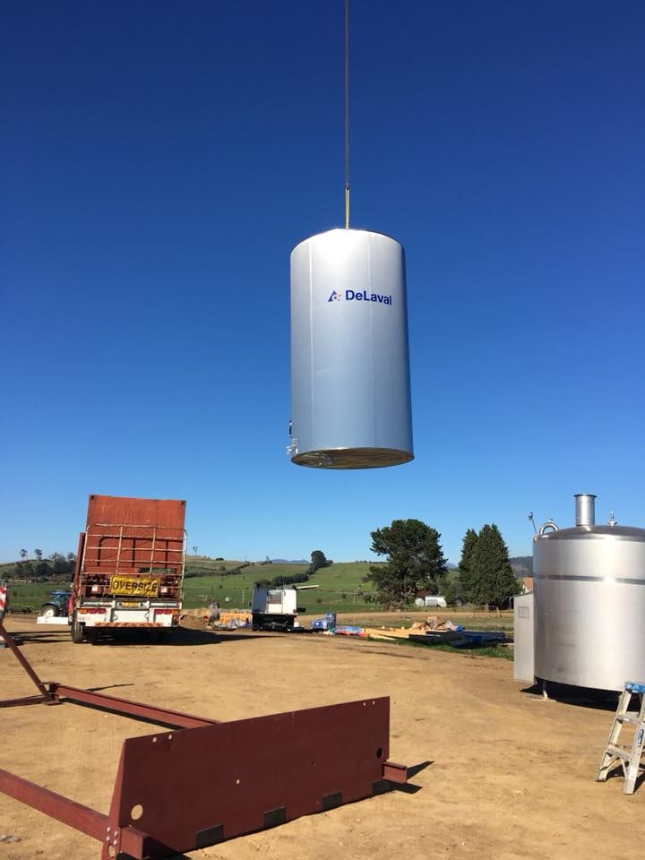 A large stainless steel tank is being lifted by a crane.