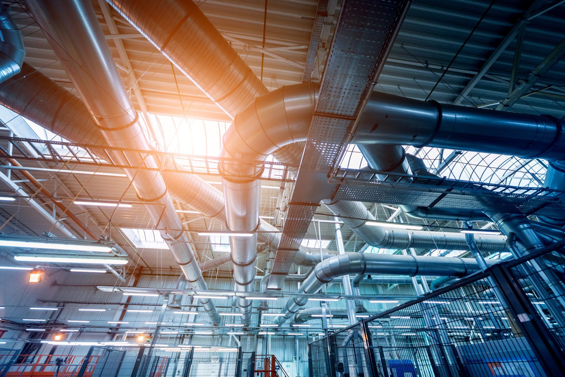 Le soleil brille à travers le plafond d'une usine avec beaucoup de tuyaux.