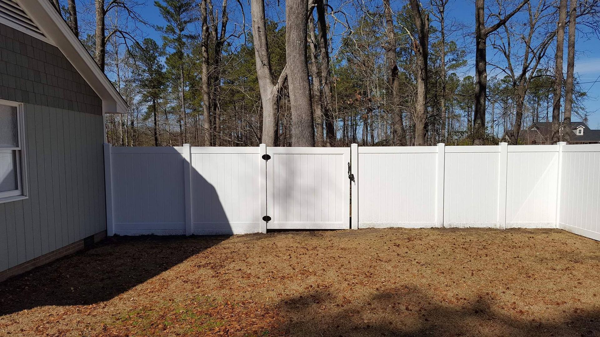 A white fence with a gate in the backyard of a house.