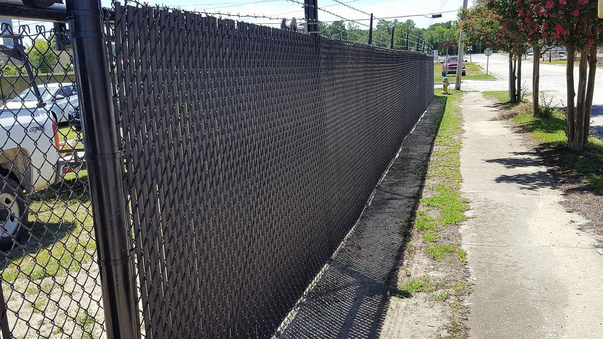 A chain link fence along a sidewalk next to a road.