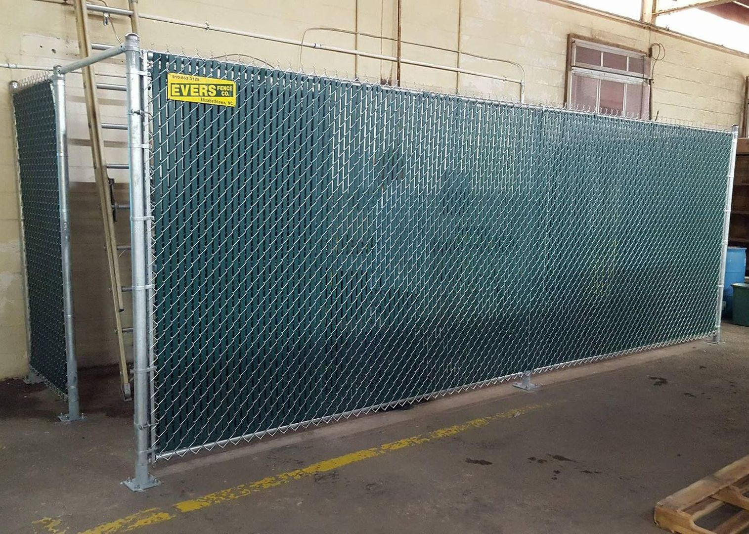 A green chain link fence with a yellow sign on it