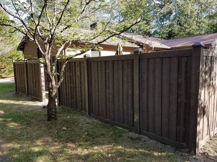 A wooden fence is surrounded by grass and trees in front of a house.