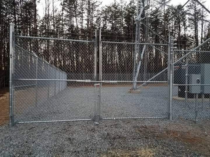 A chain link fence is surrounding a gravel area with trees in the background.