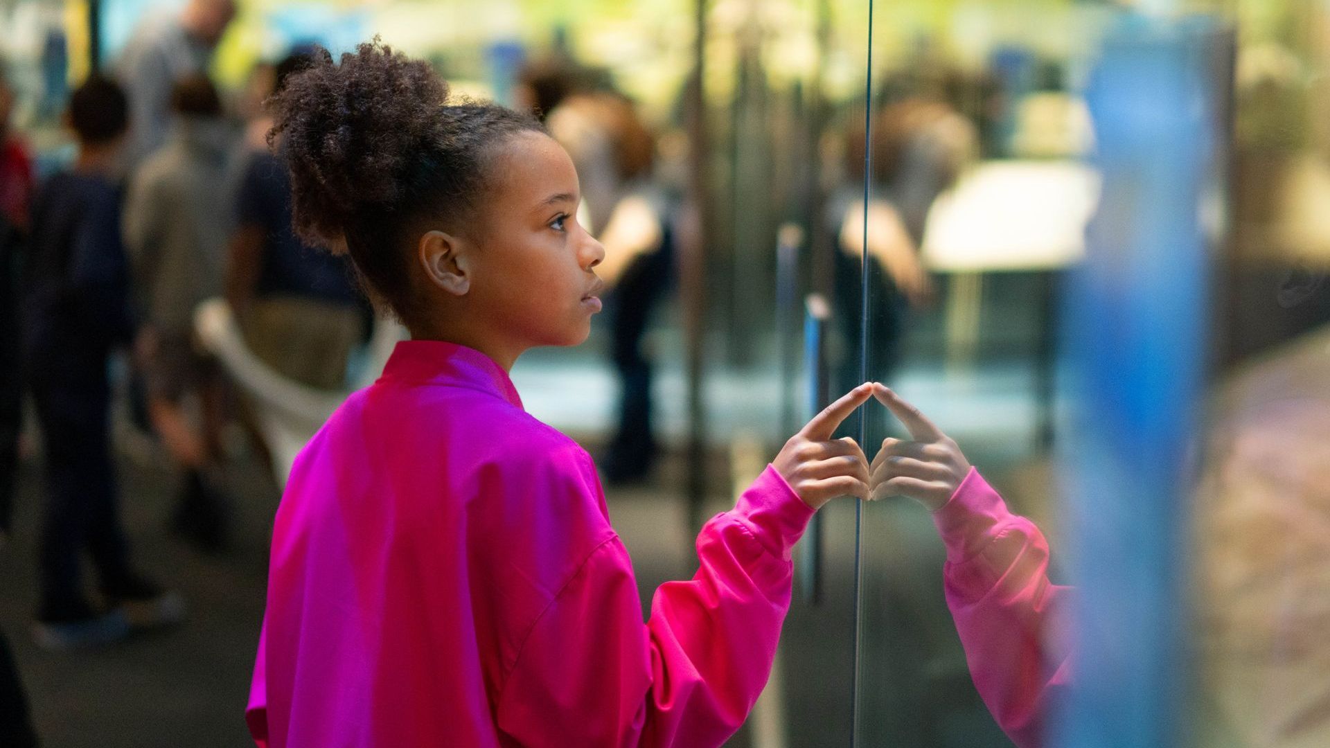 A young girl is looking at her reflection in a glass window.