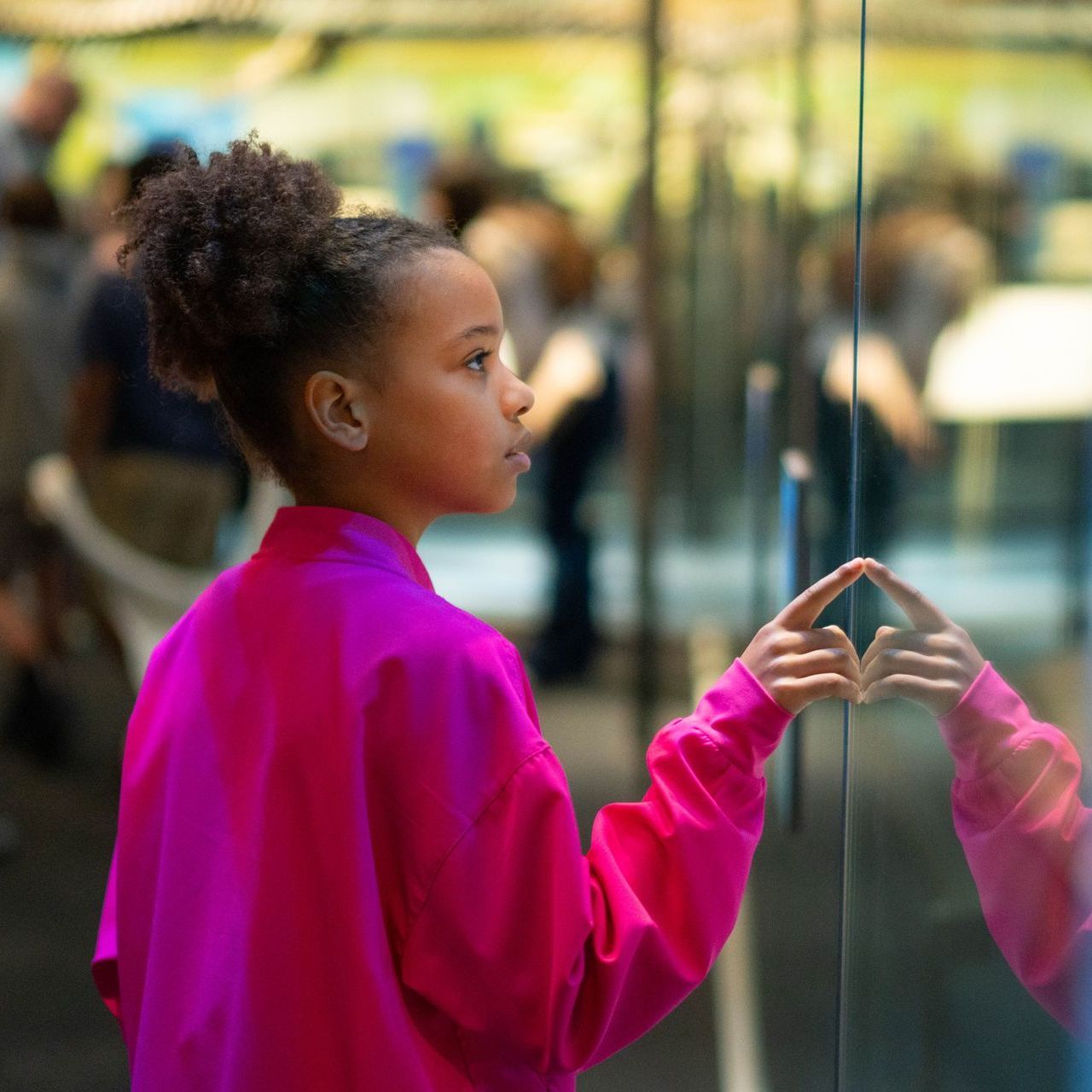 A little girl in a pink sweater is looking at her reflection in a mirror