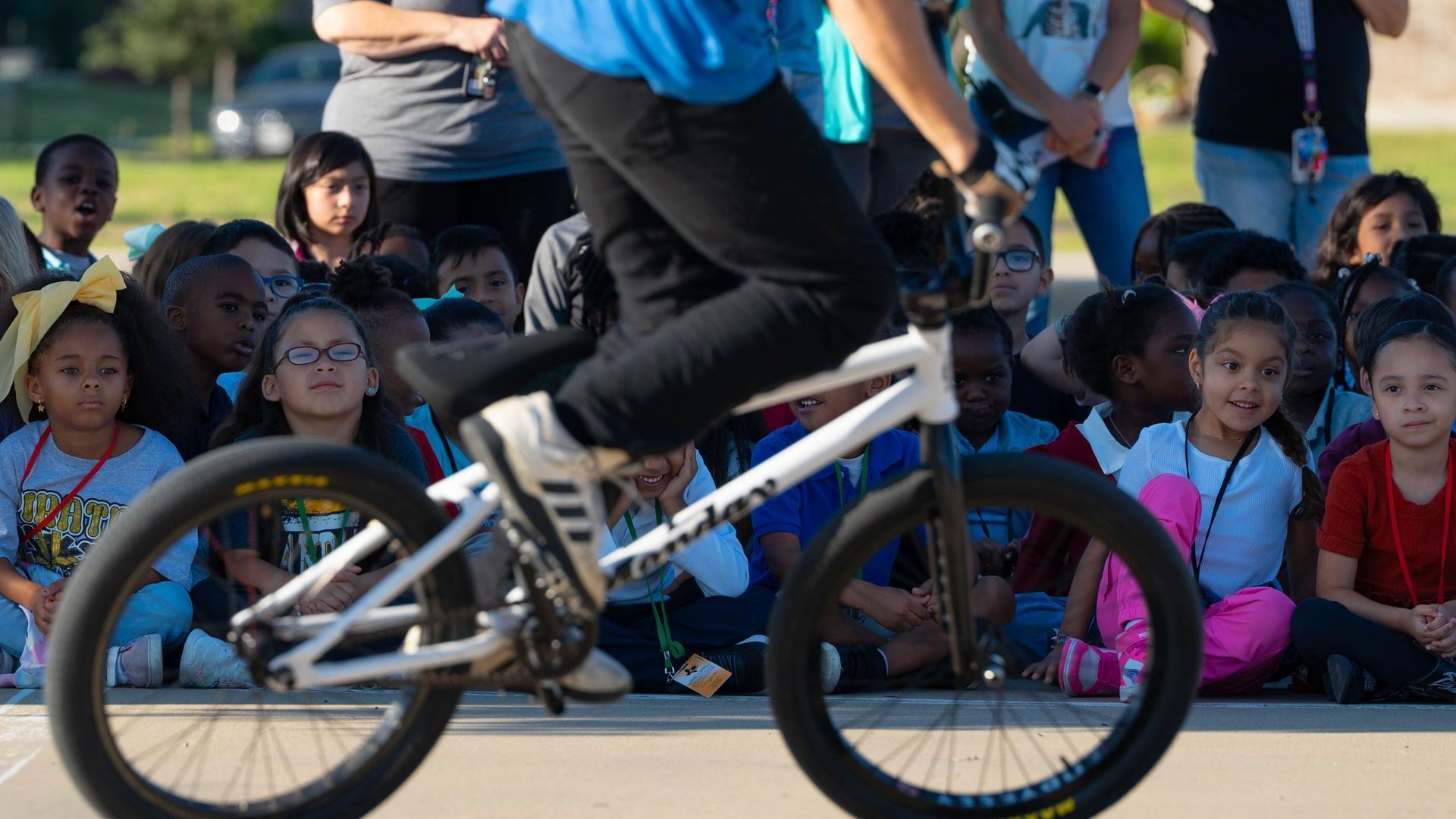 A man is riding a bike in front of a crowd of children.