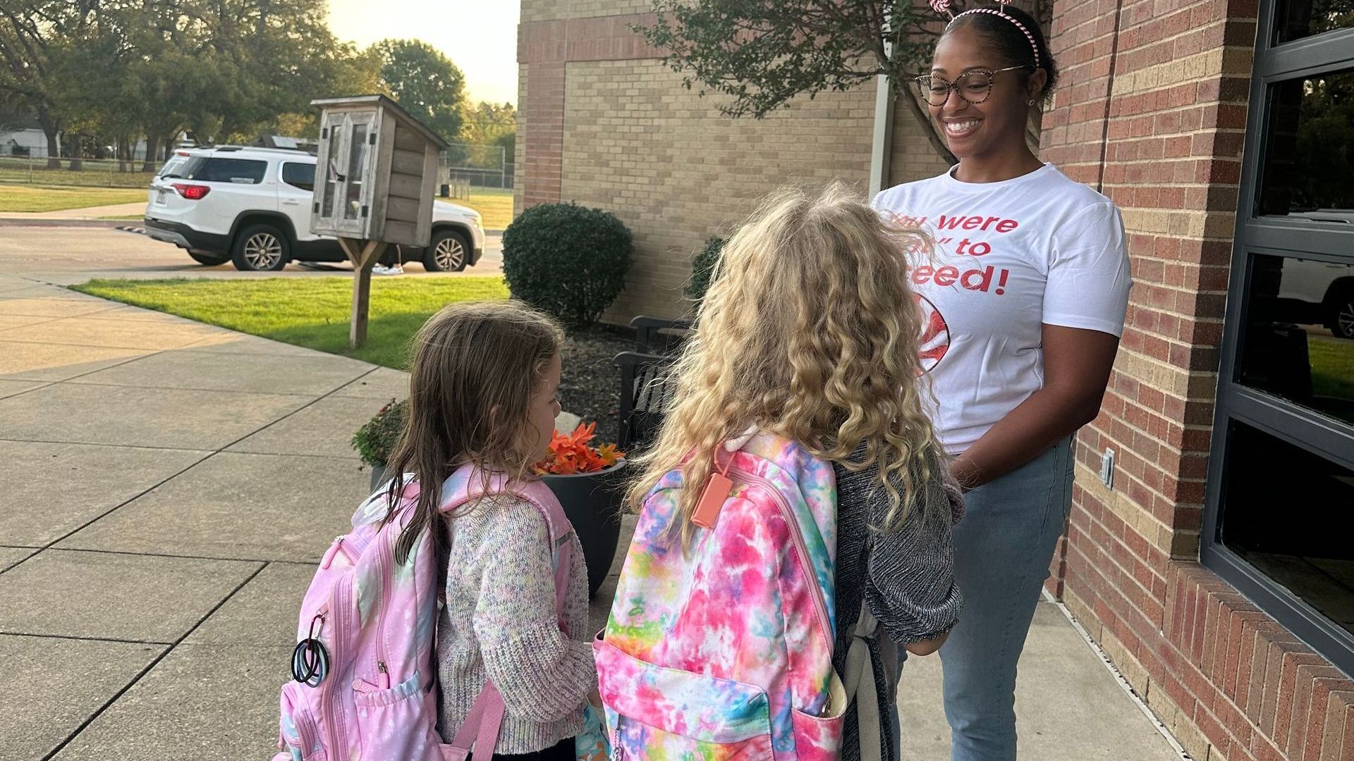 A woman is talking to two young girls on the sidewalk.