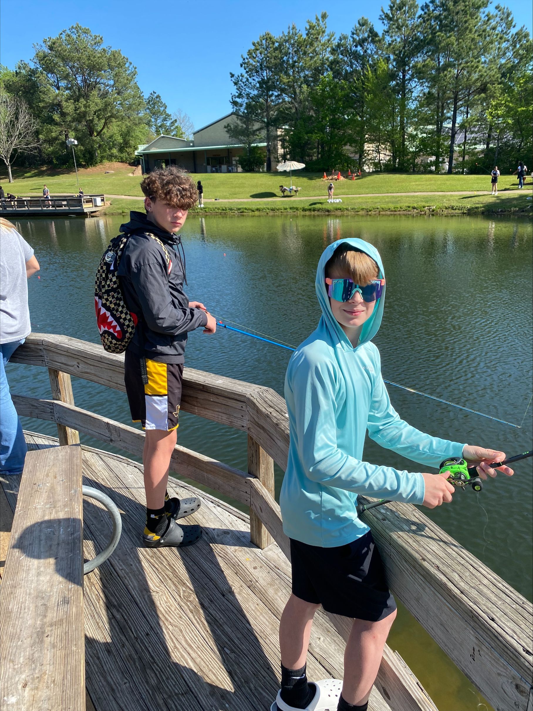 Two young boys are fishing on a pier next to a lake.