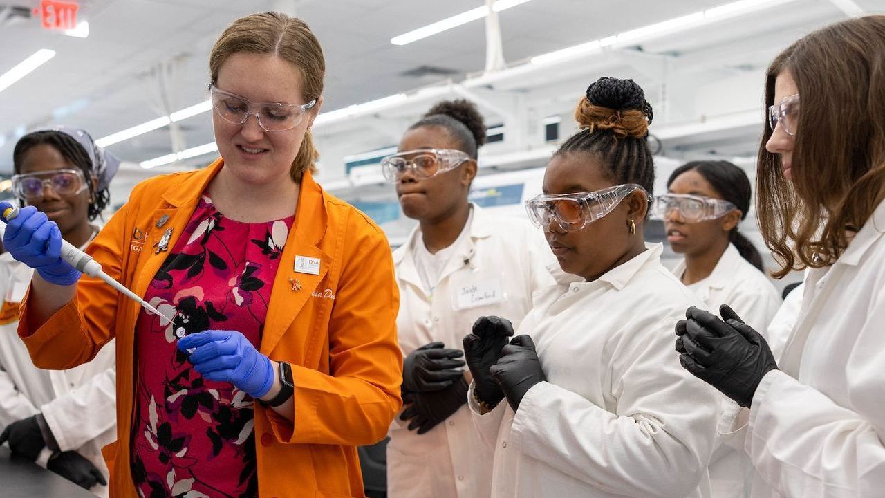 A group of women in lab coats and goggles are working in a lab.