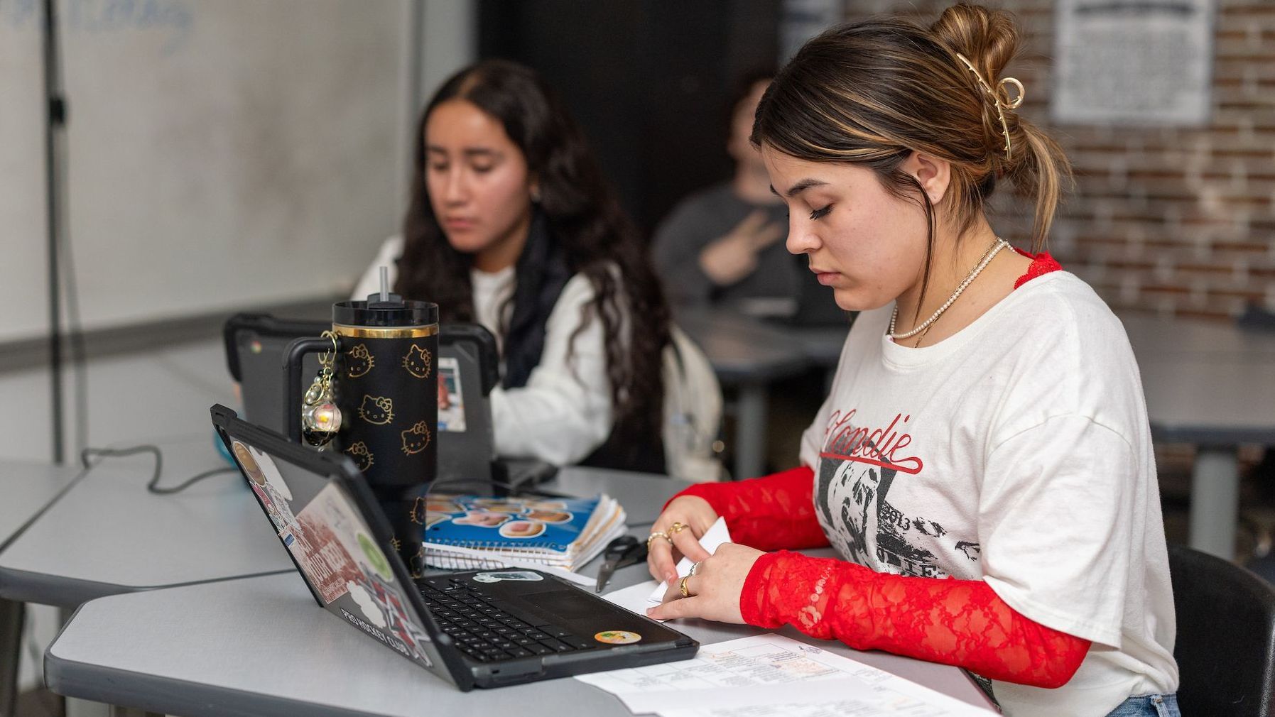 A woman is sitting at a desk using a laptop computer in a classroom.