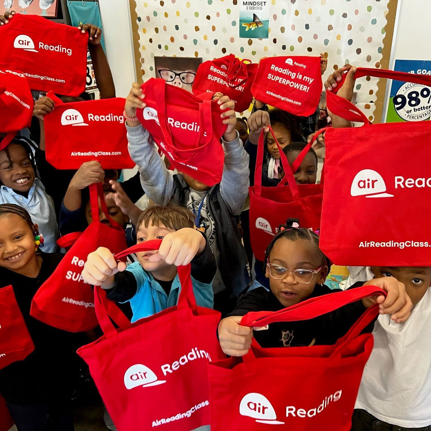 A group of children are holding up red bags that say air reading