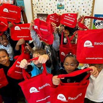A group of children are holding up red bags that say air reading
