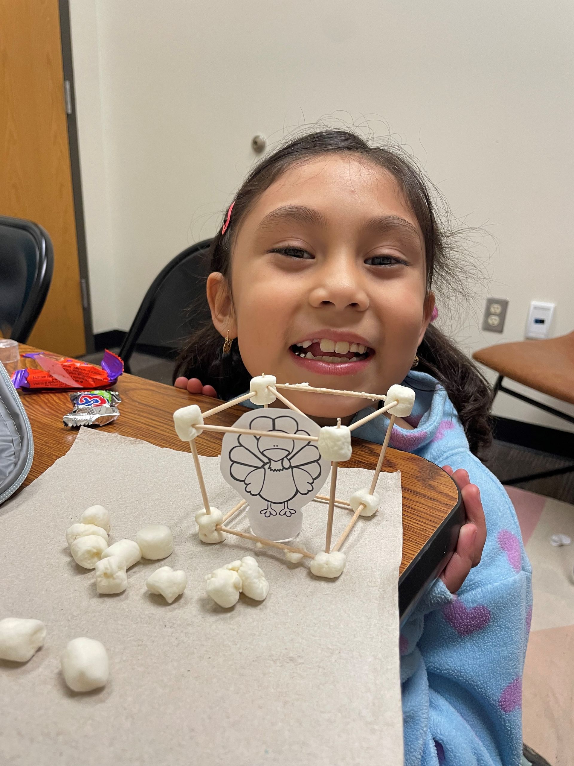 A young girl is sitting at a table holding a marshmallow sculpture.