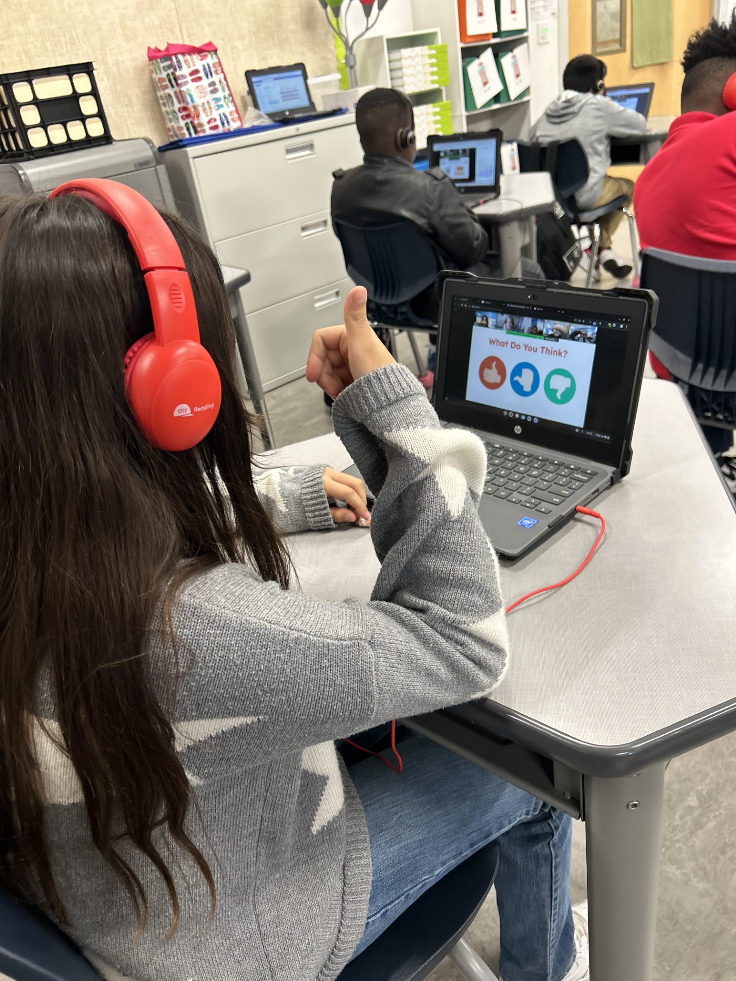 A girl wearing red headphones is sitting at a desk with a laptop.
