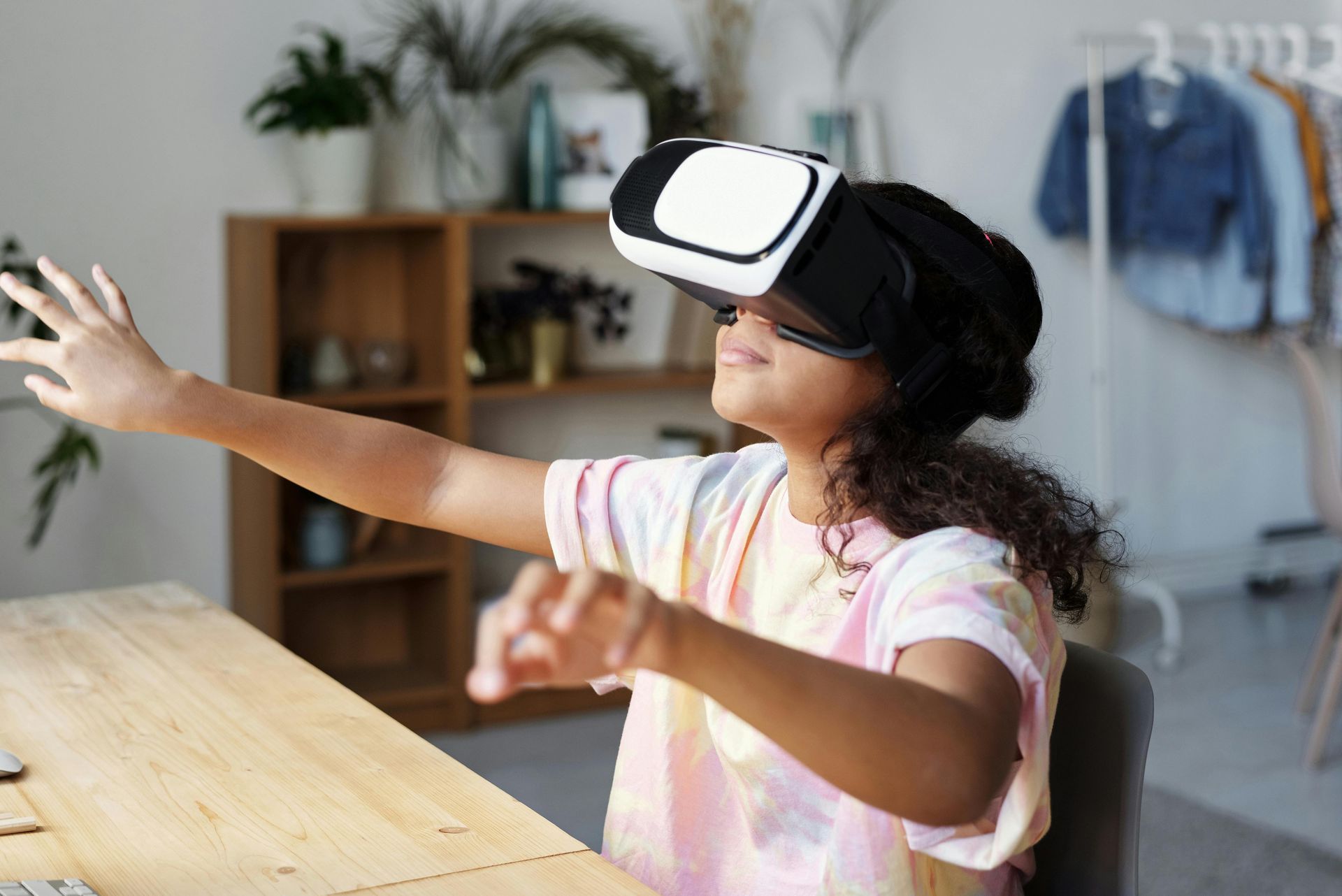 A young girl is wearing a virtual reality headset while sitting at a desk.