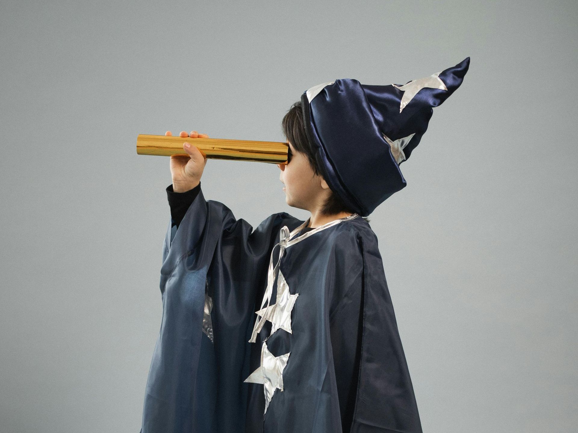 A young boy in a wizard costume is looking through a telescope.