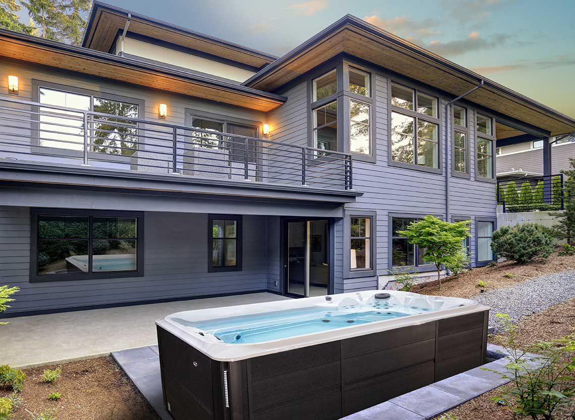 Un spa de nage est installé sur une terrasse en bois devant une maison.