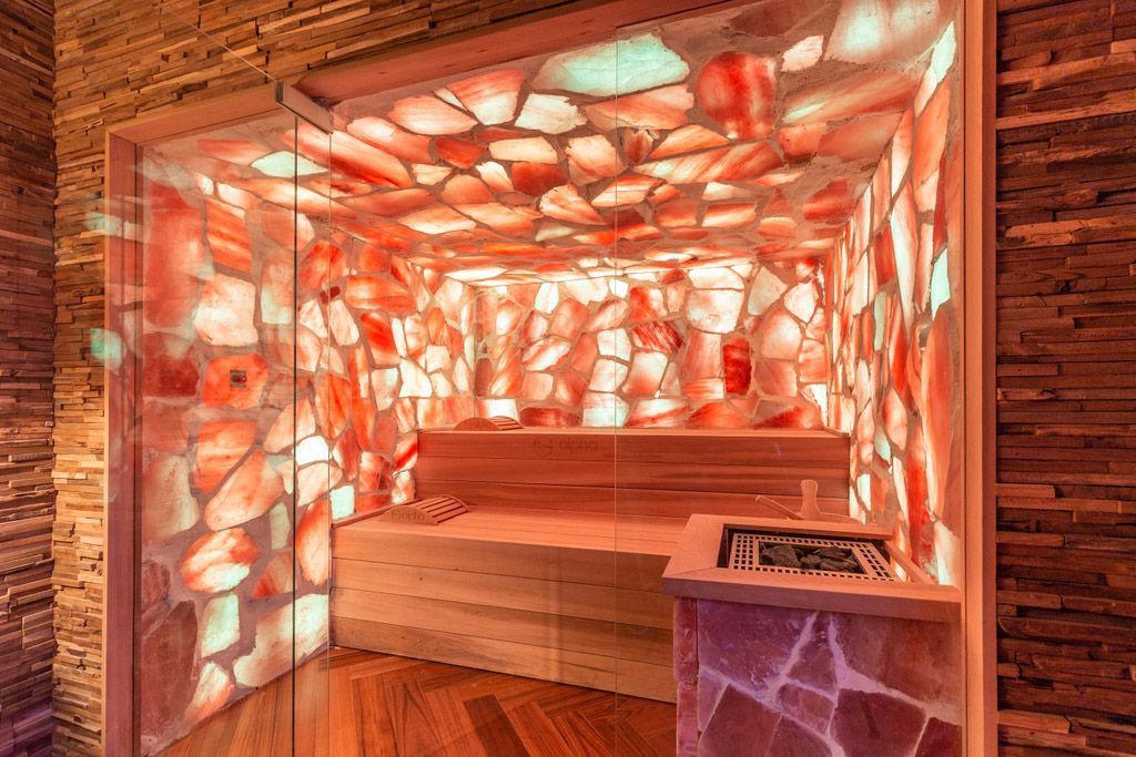 Un sauna au sel rose. Murs et plafond en cristaux de sel lumineux, banc en bois et poêle.