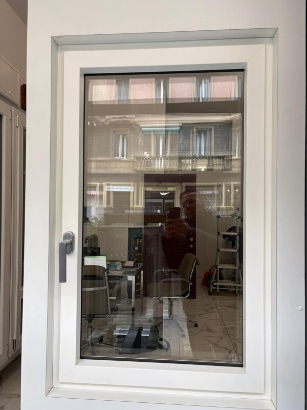 Finestra con cornice bianca su cui si riflette una stanza e degli edifici.