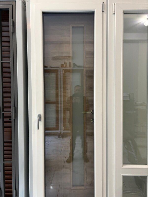 Porta con cornice bianca, pannello in vetro smerigliato e maniglia. Riflesso di una persona nel vetro.