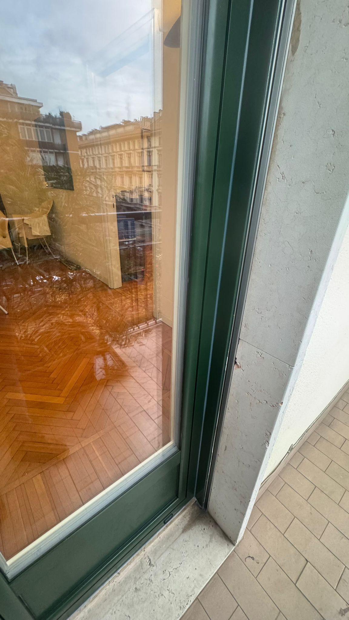 Telaio di finestra verde con rivestimento in metallo, che riflette un balcone e degli edifici.