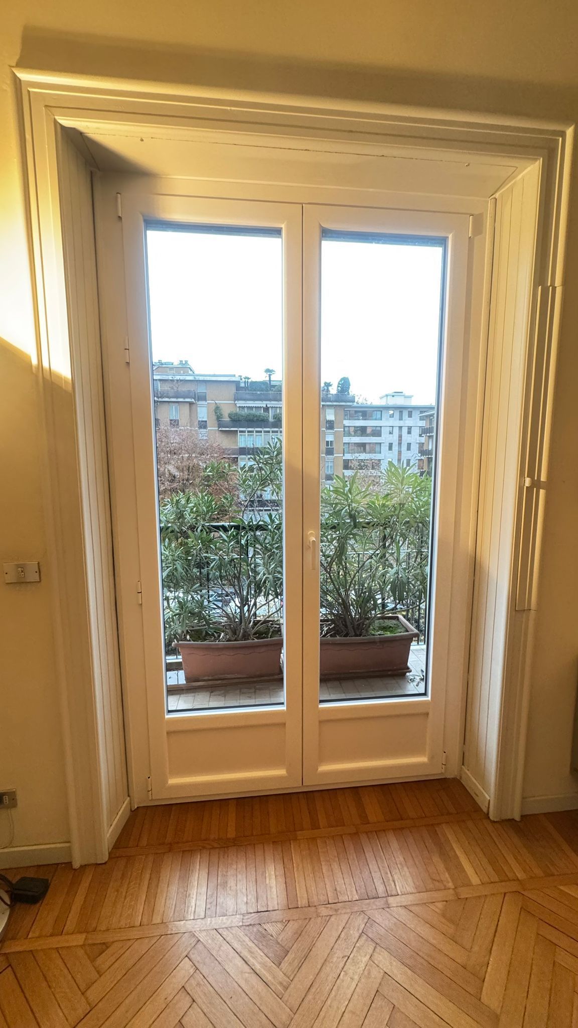 Ingresso sul balcone con piante, edifici visibili dalla finestra. 