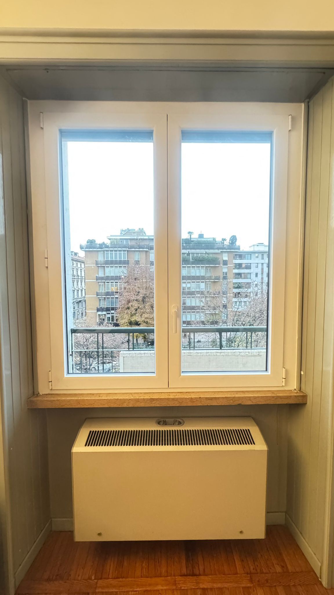 Finestra in una nicchia a muro con vista sulla città, con un termosifone bianco sotto.