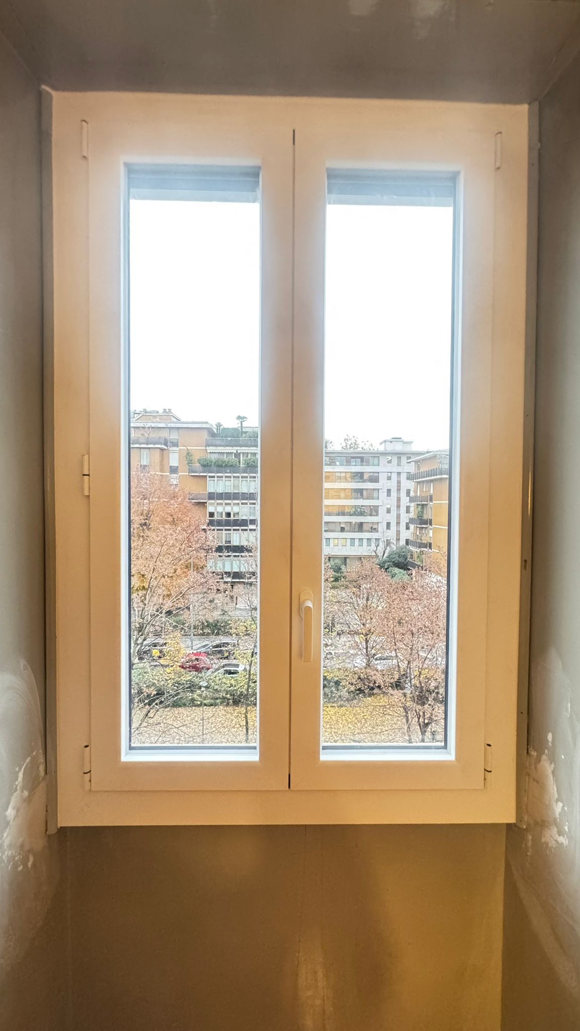 Finestra con cornice bianca che si affaccia su un paesaggio urbano alberato.