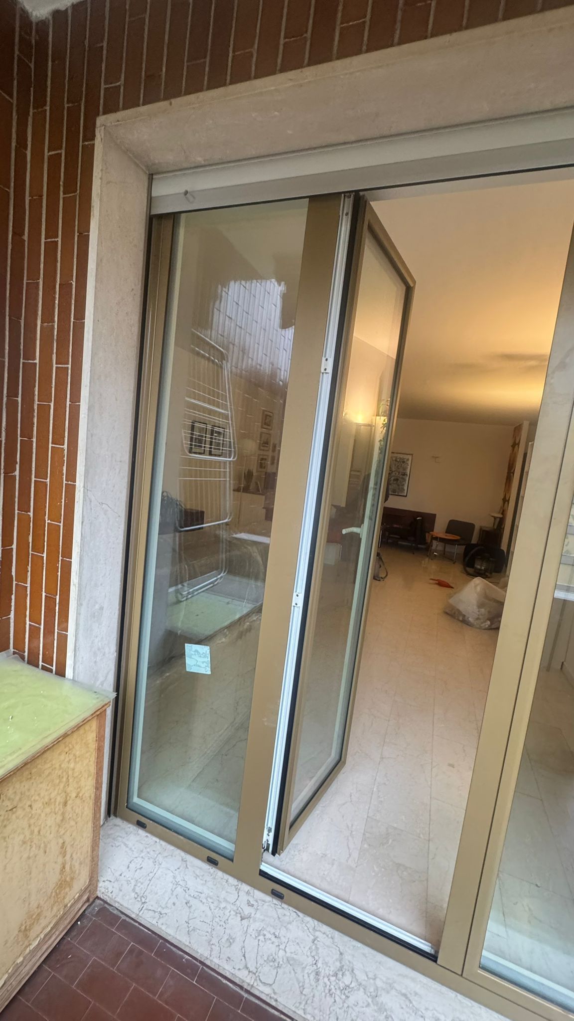 Porta a vetri aperta con telaio marrone chiaro; vista interna di una stanza con mobili.