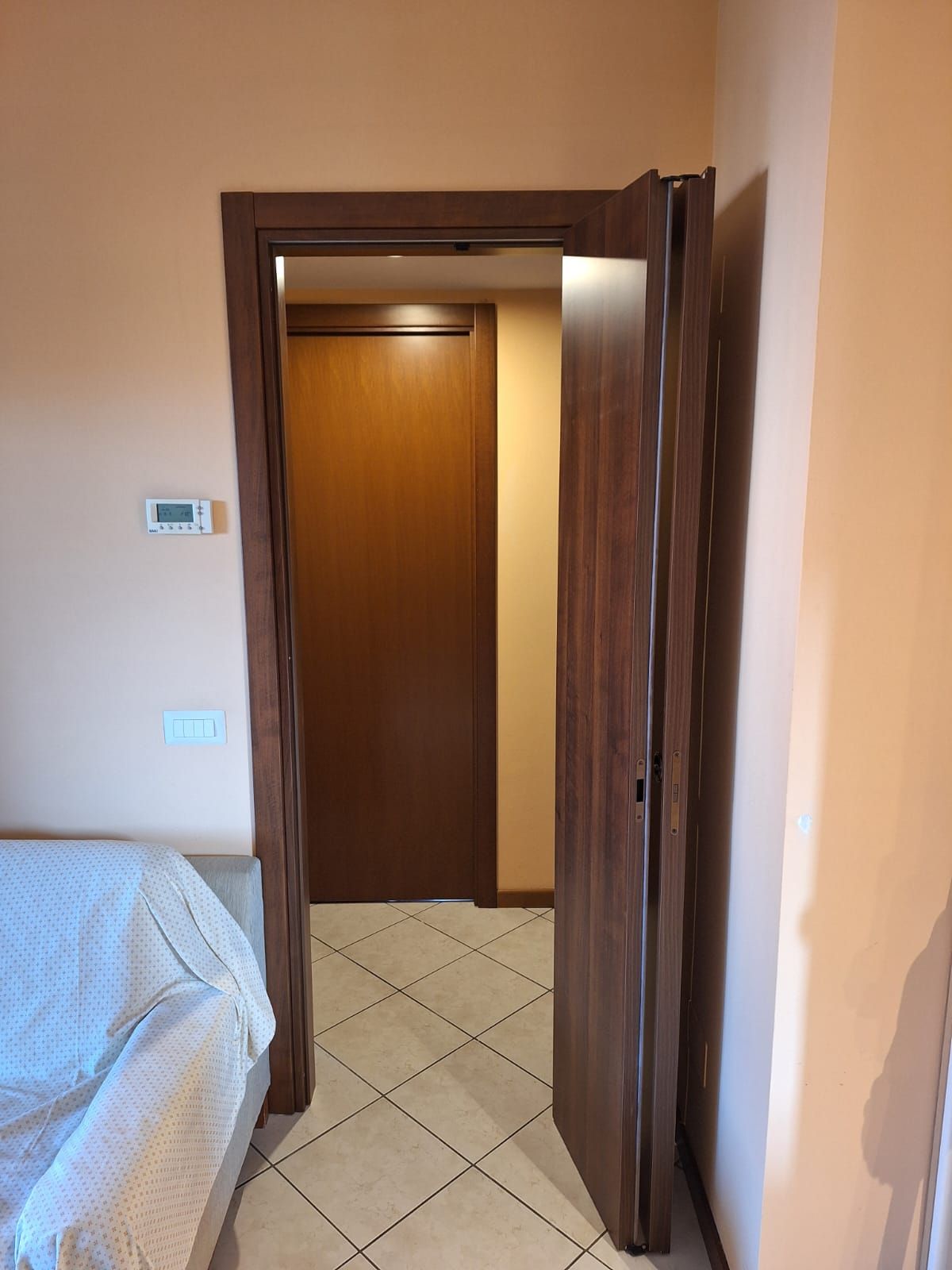 Porta aperta con finiture in legno e porta parzialmente aperta, che conduce a un corridoio con un'altra porta chiusa.