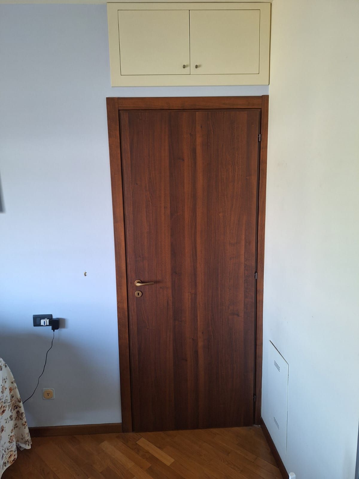 Porta in legno con un mobiletto sopra, inserita in una stanza con pareti azzurre e bianche e pavimento in legno.