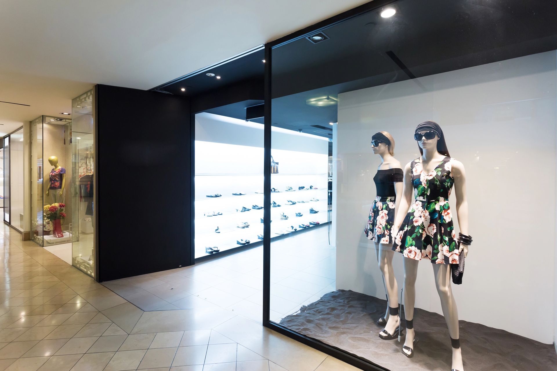 Vetrina con manichini che indossano abiti floreali e occhiali da sole, nel corridoio di un centro commerciale.