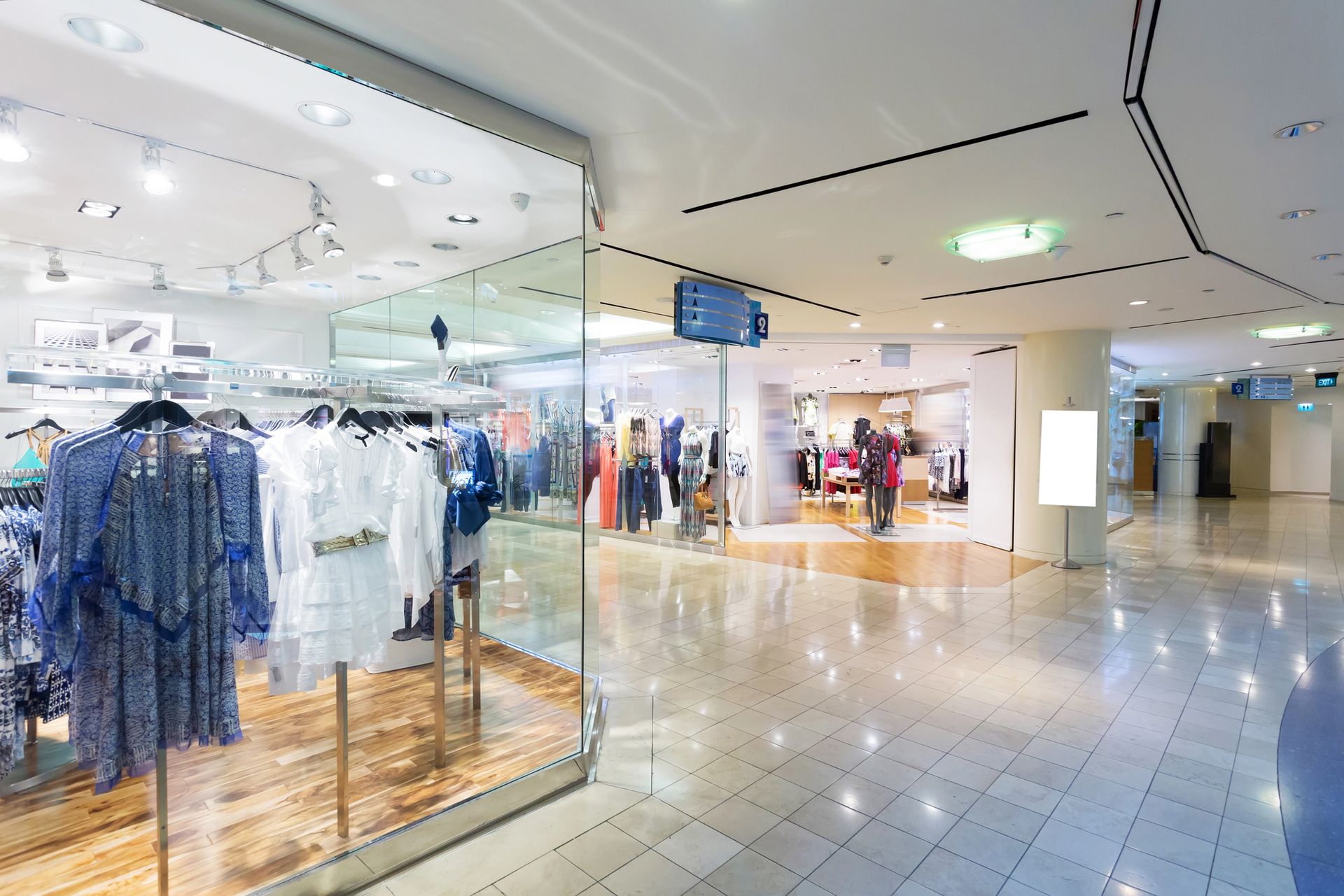 Interno di un negozio di abbigliamento con espositori di vestiti e un cartello vuoto.