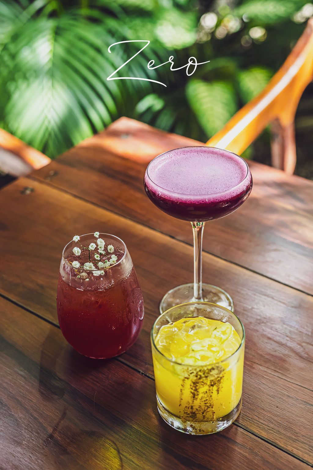 Three colorful cocktails on a wooden table outdoors. Purple, red, and yellow drinks.