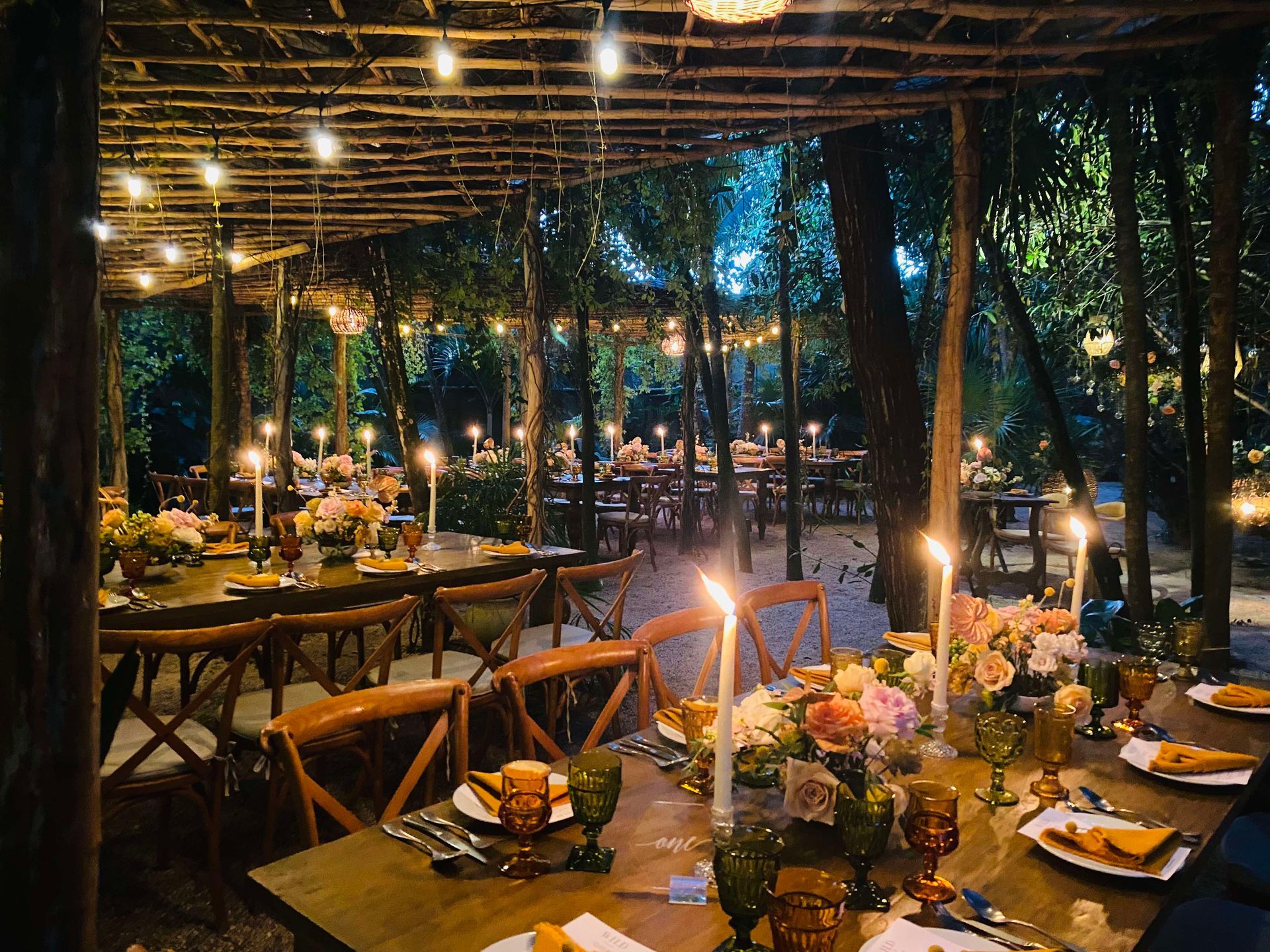 A table set for a wedding reception in the woods with candles and flowers on it 