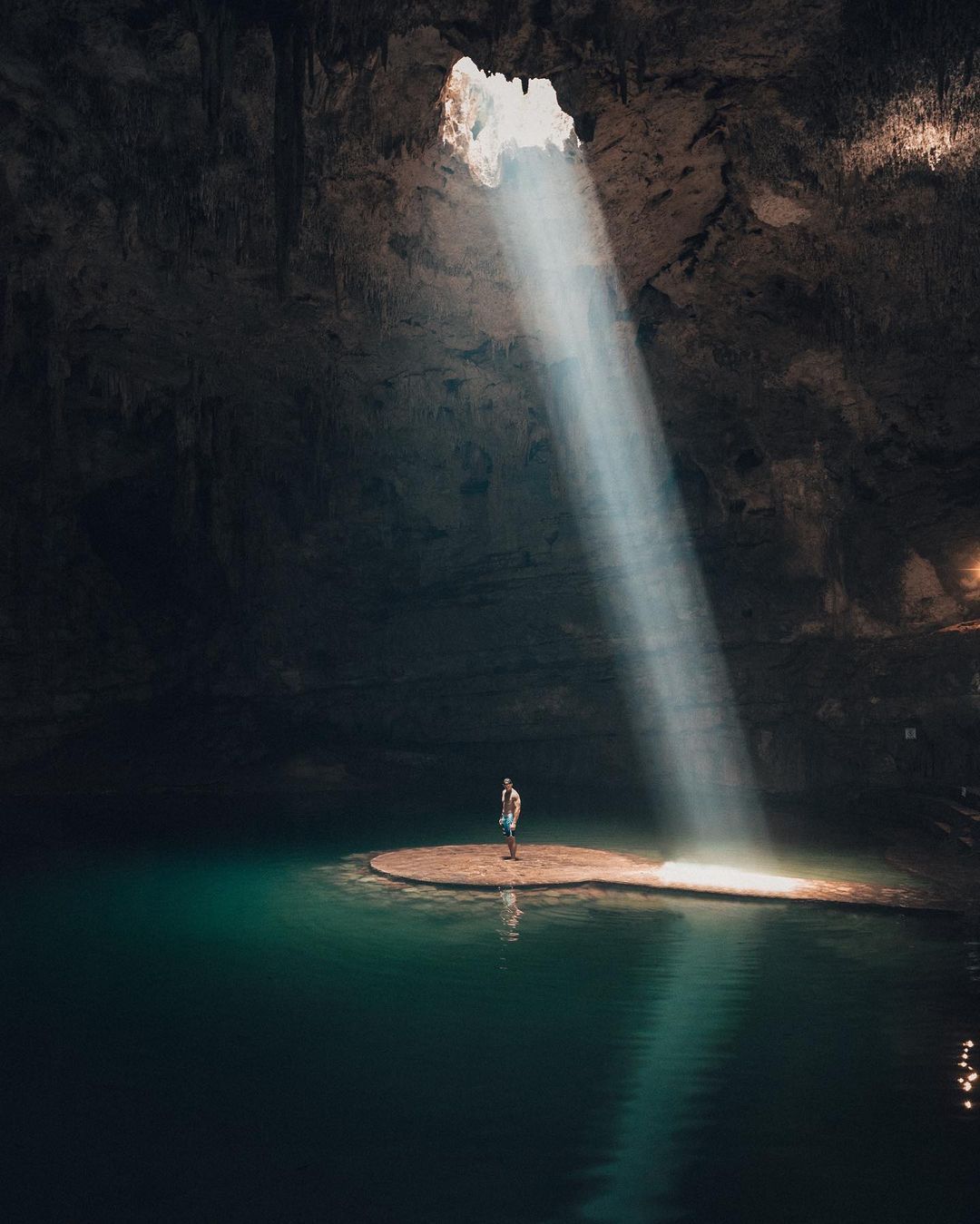 A man is standing on a small island in the middle of a cave.