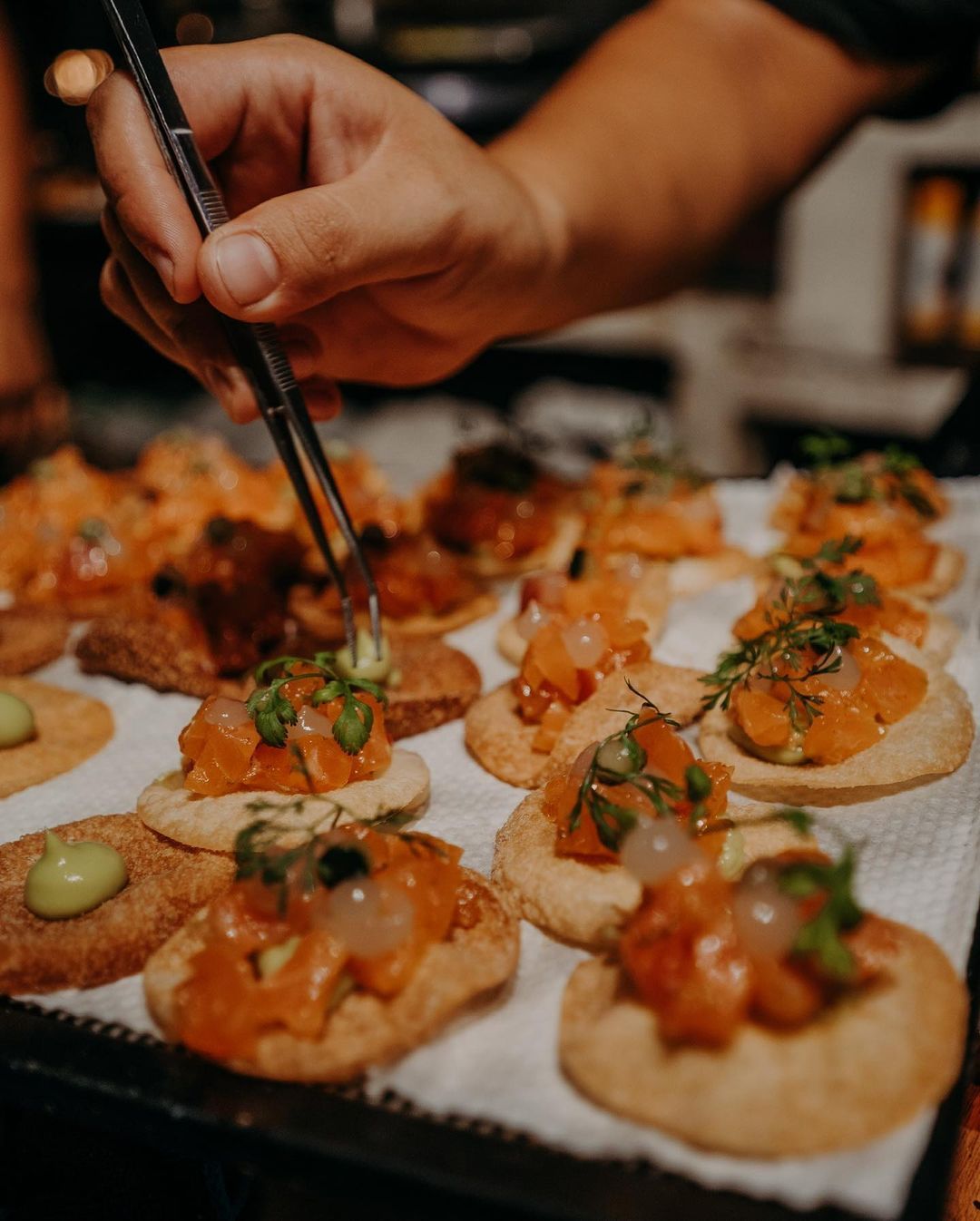 A person is holding a pair of tweezers over a tray of food.