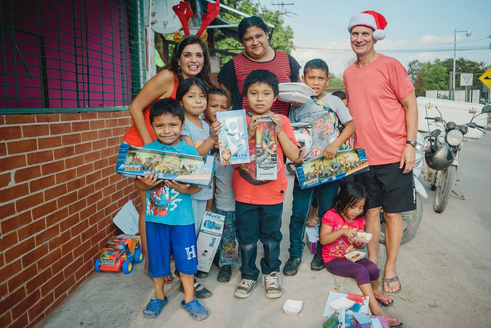 A group of people are standing in front of a brick building holding gifts.